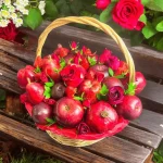 Fruit gift basket with a selection of fresh apples, plums, strawberries, pears, pomegranate, and a touch of red roses.