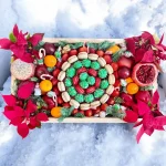 Christmas-themed wooden box with a selection of fresh fruits, chocolate covered strawberries, macarons, and festive flowers.