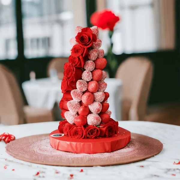 Picture of a tall, impressive tower of strawberries covered in smooth white chocolate, set against a backdrop of fresh roses, enhancing its visual allure.