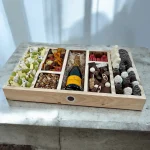 A beautifully arranged gift box with a selection of cheeses, nuts, and a variety of chocolate-covered fruits.