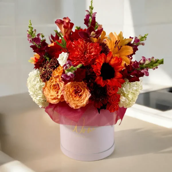 A fall-inspired floral display with a variety of yellow, orange, and red flowers, set against a wooden background.