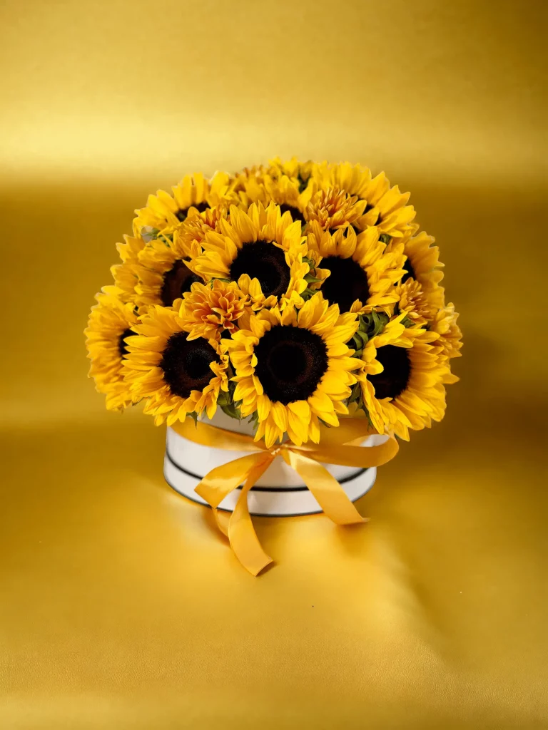 Picture of a sunflower-filled hatbox sitting on a table, highlighting the dense and cheerful arrangement of yellow blooms