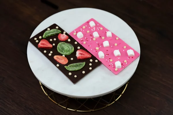 Image of artisanal chocolate bars: dark chocolate with dried kiwi & strawberries, and pink white chocolate with marshmallows.
