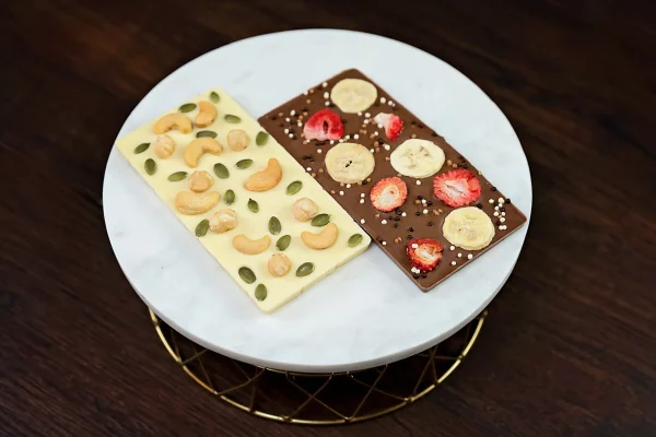 Image of two artisanal chocolate bars: creamy white chocolate with nuts and sweet milk chocolate with freeze-dried bananas and strawberries.