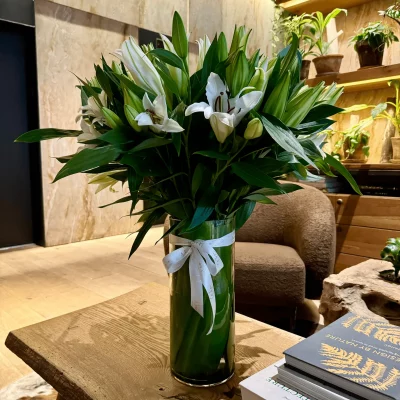 Side view of white lilies and greenery in a sleek vase.