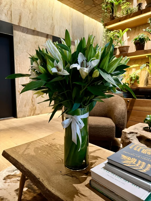 Side view of white lilies and greenery in a sleek vase.