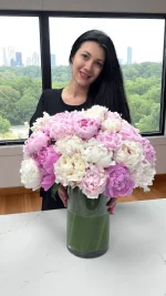 Close-up of a woman holding a bright floral bouquet in a vase, showcasing pink peonies, roses, and mixed flowers from WOWBouquet
