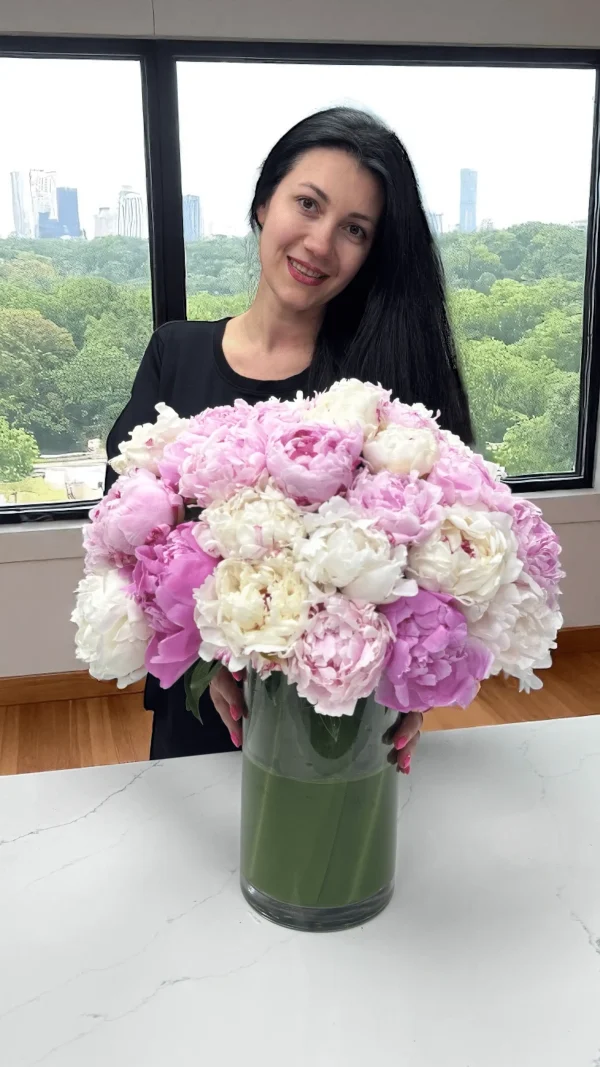 Close-up of a woman holding a bright floral bouquet in a vase, showcasing pink peonies, roses, and mixed flowers from WOWBouquet