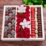 A gift box with chocolate-covered strawberries, red roses, and assorted French macarons.