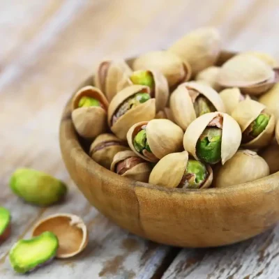 Opened pistachio shells revealing vibrant green nuts inside, highlighting their mild sweetness and nutty taste.