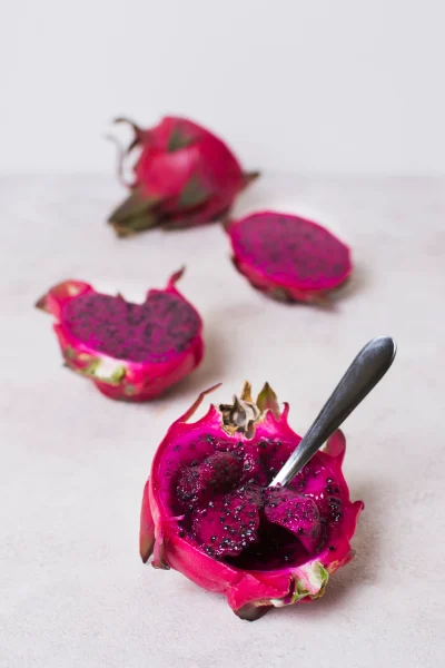 A spoon scooping out the soft, juicy flesh of a dragon fruit, revealing its speckled white interior.