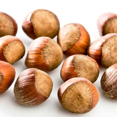 A close-up of whole and shelled hazelnuts, showing their small, round shape with a rich brown shell.