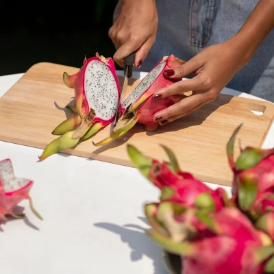 Hands slicing a dragon fruit in half, revealing its speckled white flesh inside the vibrant pink rind.