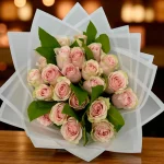 Two dozen pink roses wrapped in designer paper with greenery