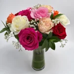 Close-up of fresh assorted roses in pink, red, yellow, and white with decorative greenery in a glass vase.