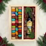 Gourmet macaron and chocolate gift box displayed with holiday greenery and candles